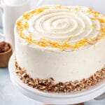 Cream cheese frosted carrot cake decorated with chopped pecans and orange zest