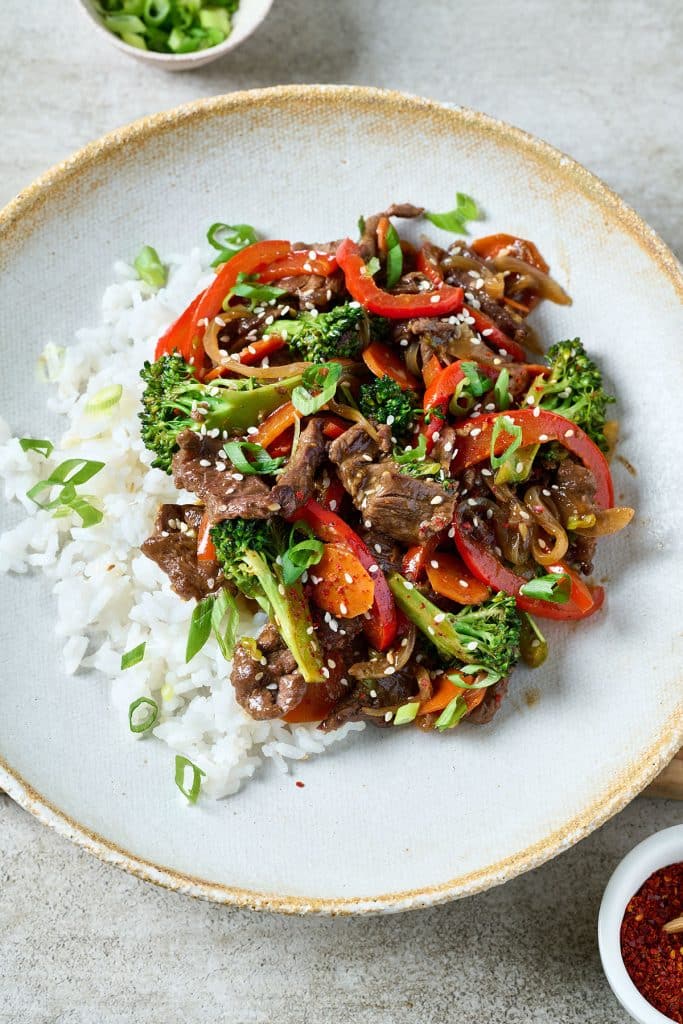 beef stir fry with white rice on a white plate.