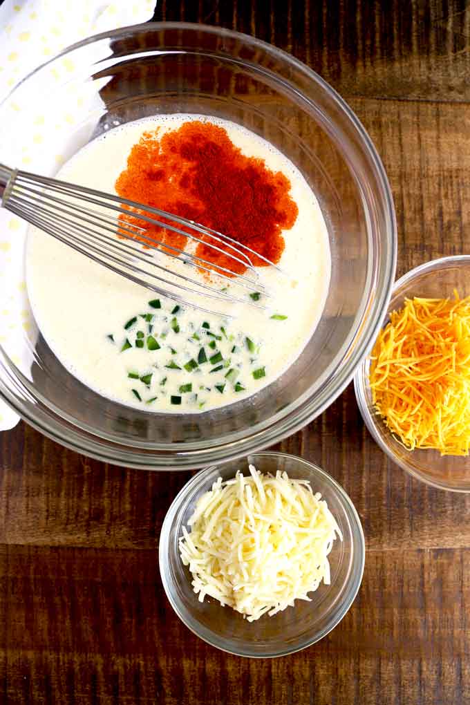 Eggs and Half and Half mixture, chopped jalapenos and paprika in a mixing bowl