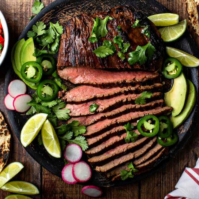 sliced authentic grilled carne asada with cilantro and avocados in a black plate