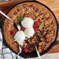 top view of a chocolate chip skillet cookie with three scoops of vanilla ice cream and garnished with raspberries and mint leaves