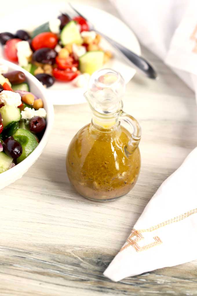 A small container with Greek dressing on a white wooden surface.