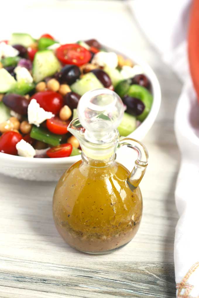 Greek Dressing in a small dressing jar next to a bowl of salad