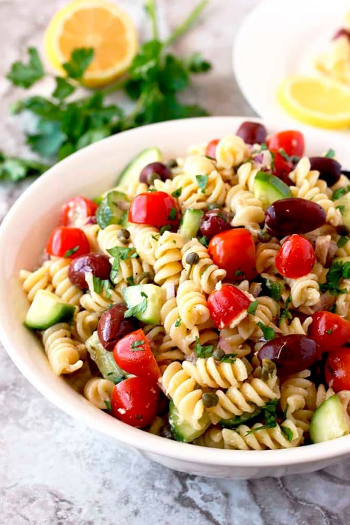 Mediterranean Tuna Pasta Salad with tomatoes, Kalamata olives, cucumbers, chopped onions and capers served on a white bowl
