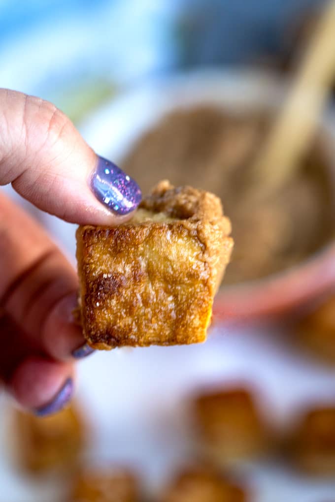 Hands holding a golden brown crispy oven baked tofu piece.