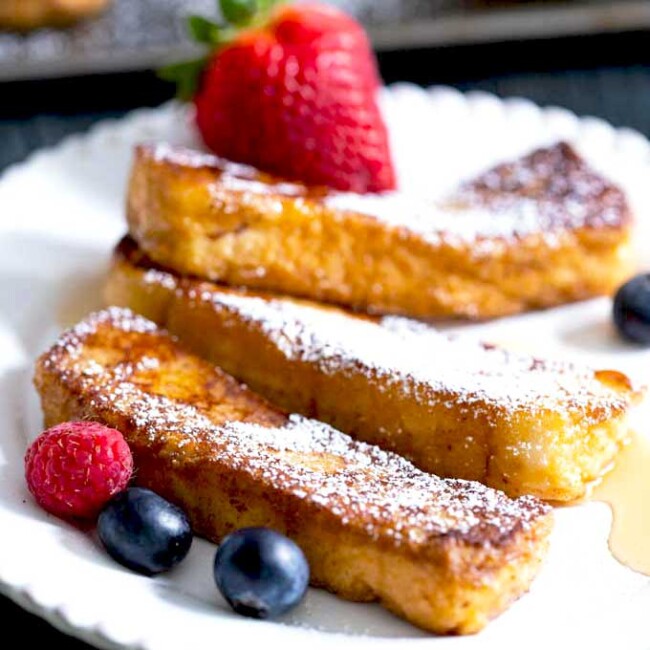 Cinnamon French Toast Sticks served on a white plate with berries and maple syrup.