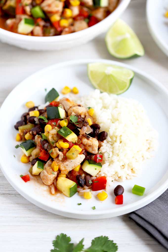 Hearty Chicken Stew with corn and black beans served with white rice on a white plate.