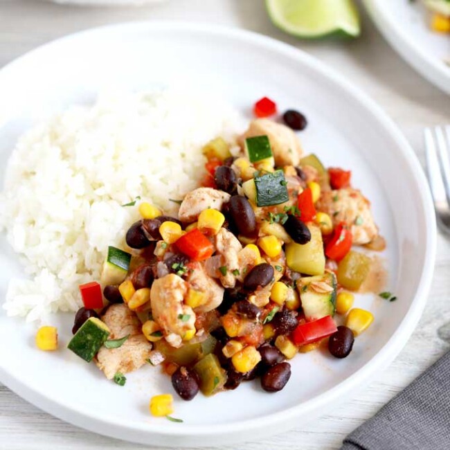 Hearty Chicken Stew with corn and black beans served with white rice on a white plate.
