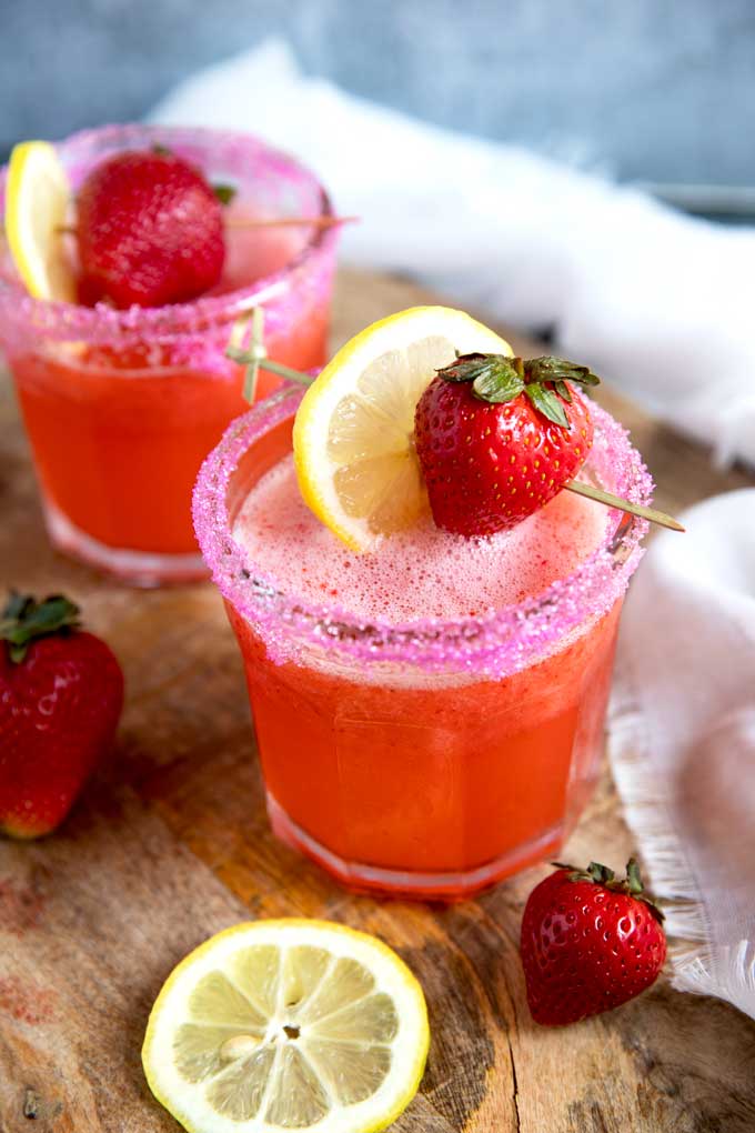 Two glasses of refreshing Strawberry Lemonade Vodka Cocktail garnished with fresh strawberries and lemon slices on a wooden surface