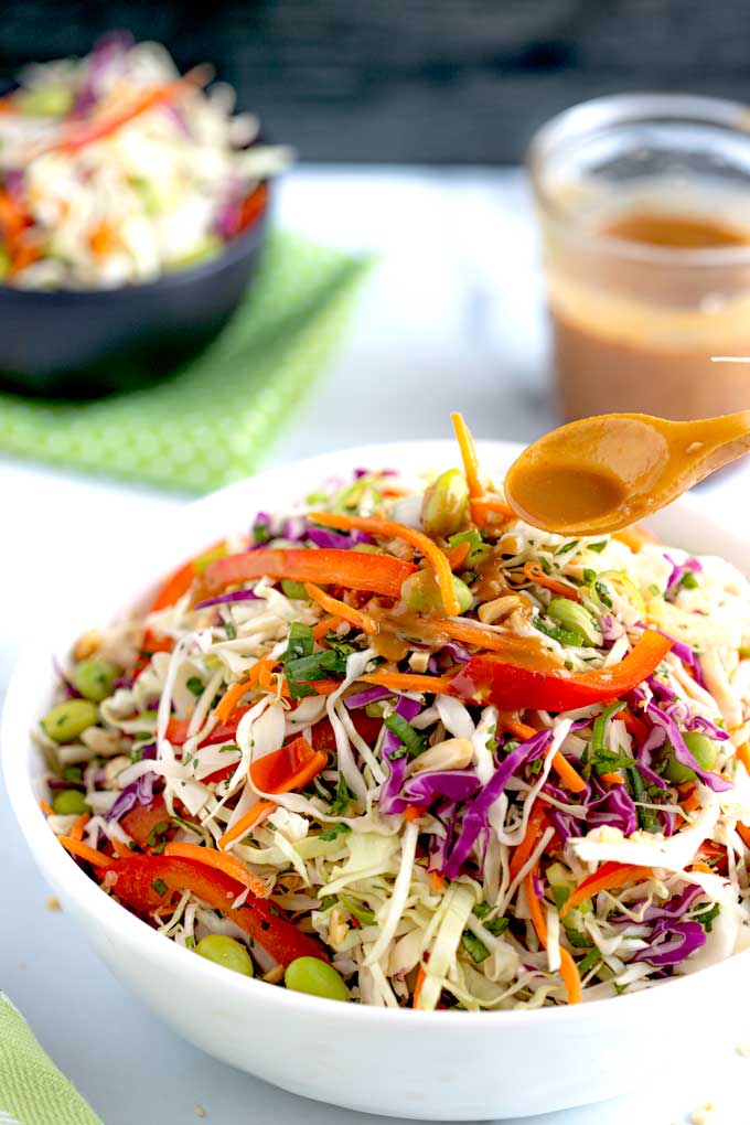 A bowl coleslaw getting drizzled with Peanut dressing.