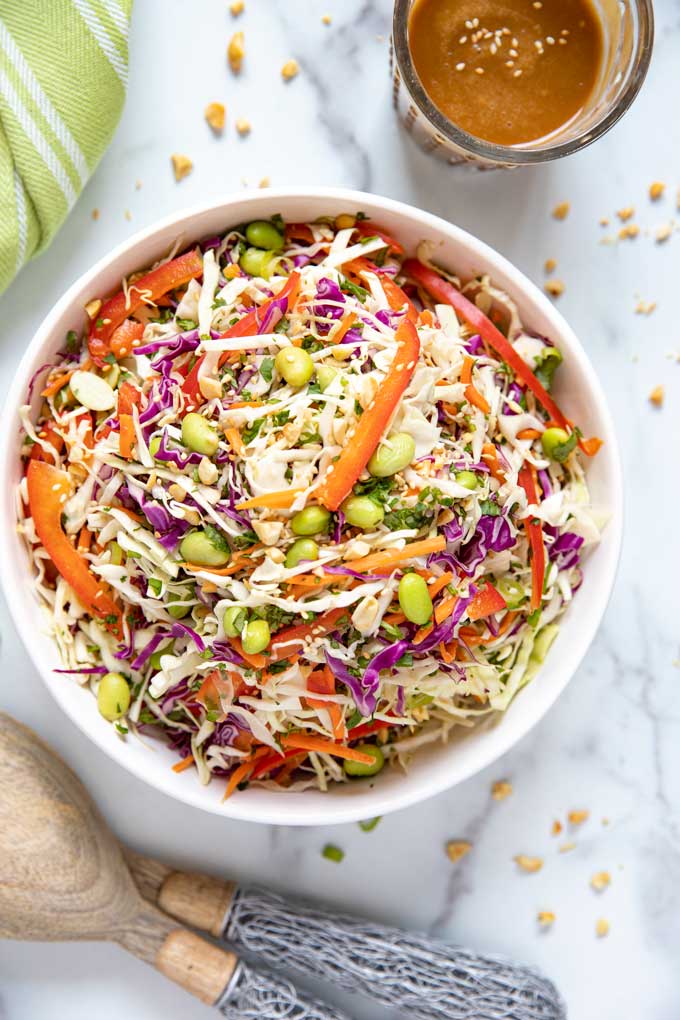 Top view of a bowl filled with Asian Coleslaw next to a container filled with Ginger Sesame Peanut Dressing.