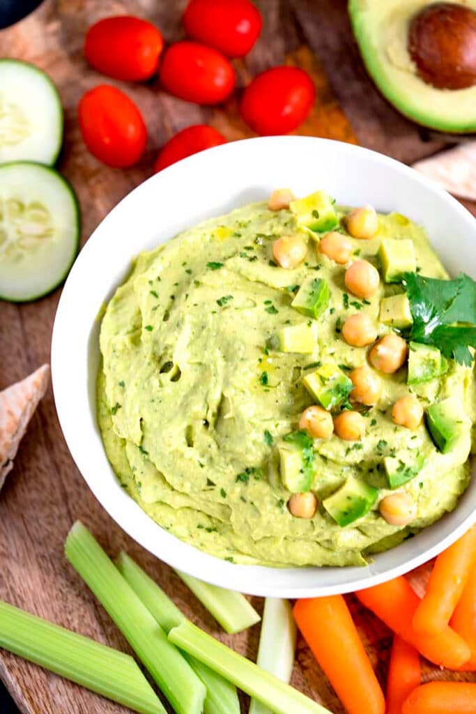 Top view of hummus topped with avocado pieces, chickpeas and cilantro.