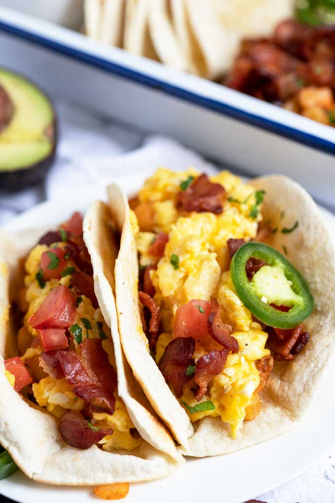 Two tacos loaded with potatoes, cheesy scrambled eggs, bacon and topped with tomatoes and jalapenos.