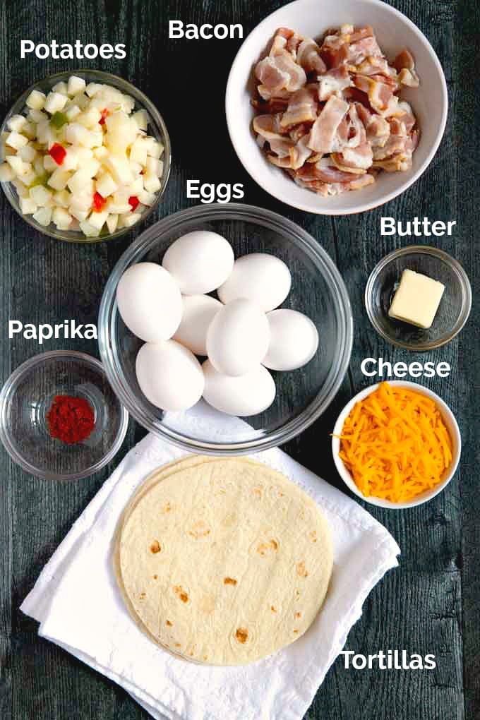 Ingredients to make this breakfast recipe on a dark surface. Eggs, potatoes, cheese, bacon, paprika, butter, tortillas.