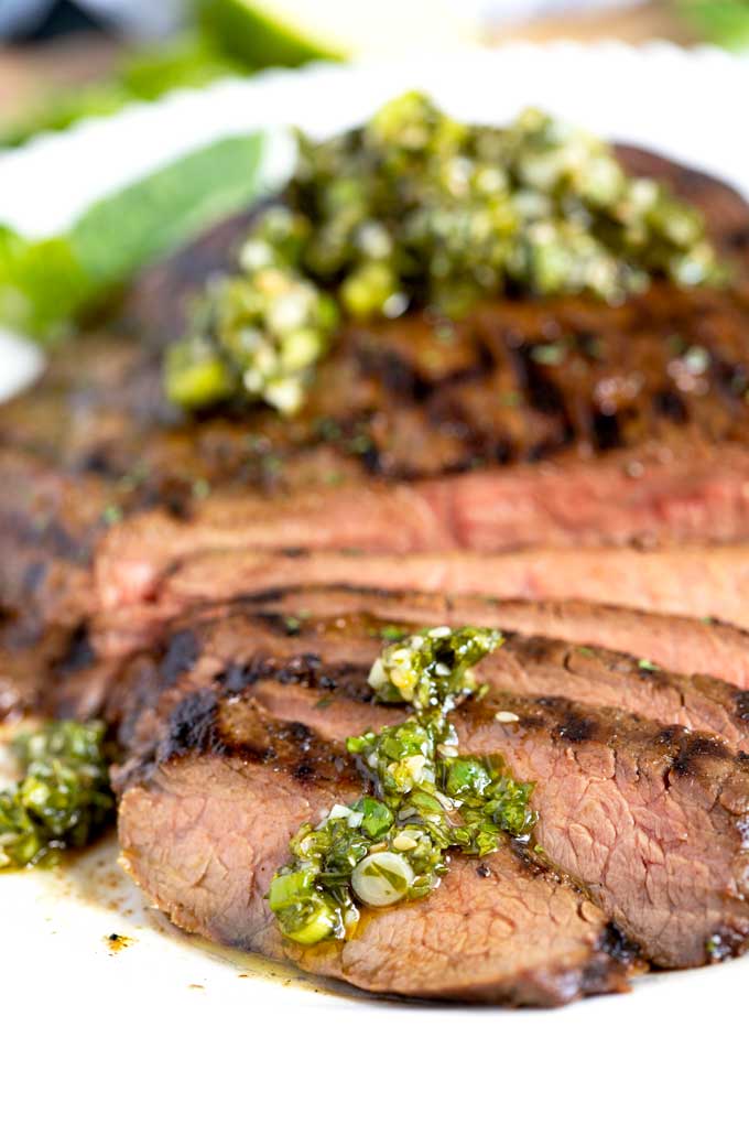 Close up view of sliced grilled steak topped with cilantro basil Asian chimichurri.
