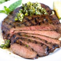 Grilled steak sliced and top with Asian chimichurri on a white plate.