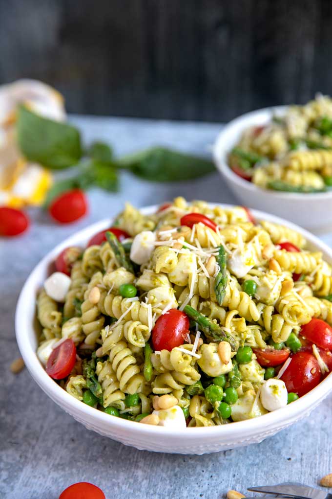 A white bowl filled with Pesto Pasta Salad with asparagus, peas, mozzarella tomatoes and Parmesan