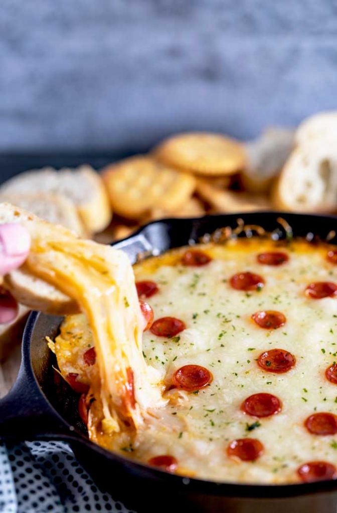 Gooey cheese is pulled from the skillet dip with a piece of bread