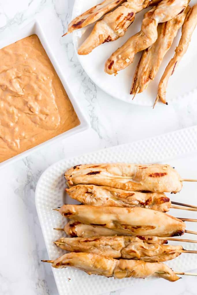 Plates of Chicken Satay next to a bowl of peanut dipping sauce