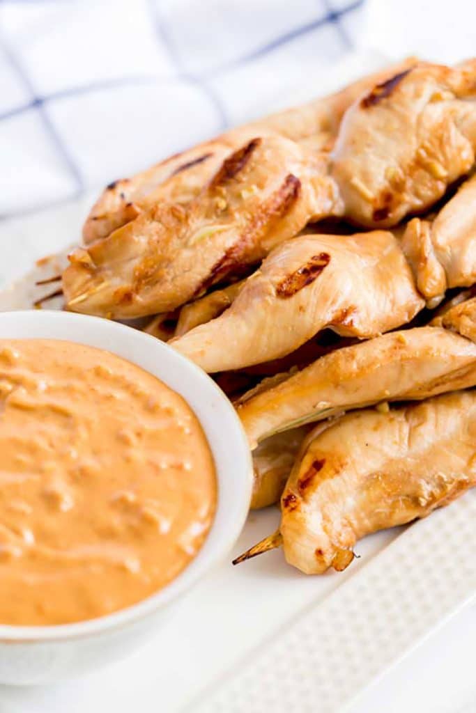 Chicken skewers on a plate next to a bowl of Thai dipping sauce.
