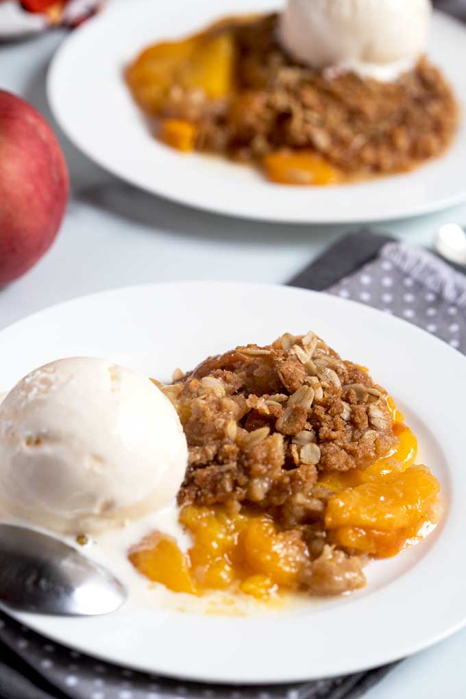 Baked peach crisp topped with vanilla ice cream on a white plate