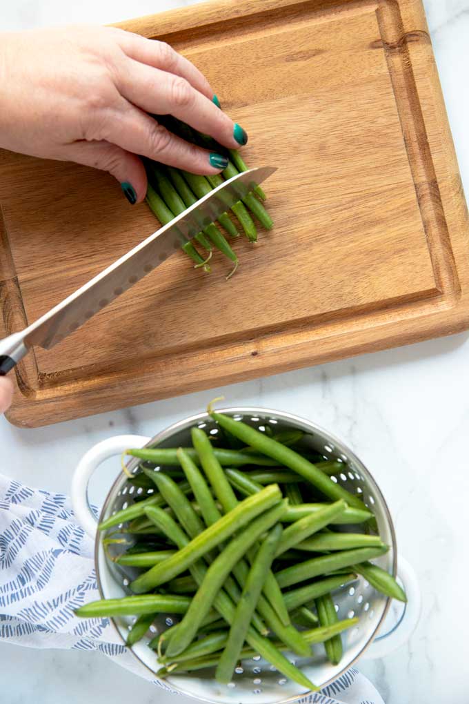 Green beans getting trimmed on a cutting board.