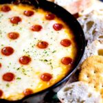 A skillet filled with cheesy pizza dip served with bread and crackers