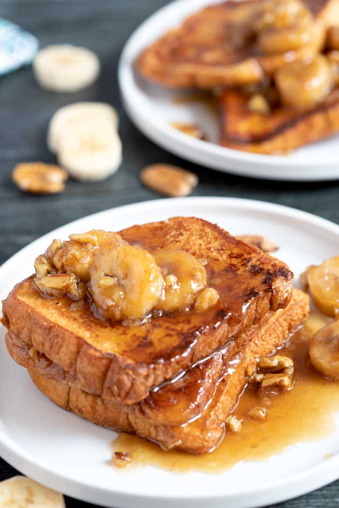 Three slices of French toast with bananas and pecans on a white plate