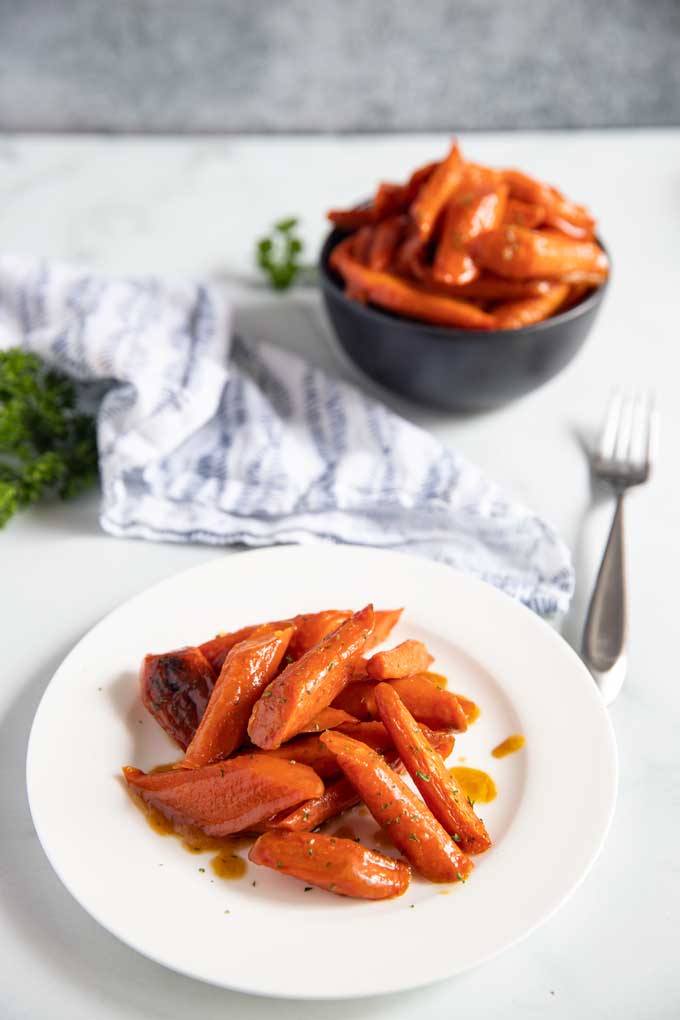 Dos porciones de horno zanahorias en un plato blanco y negro tazón.