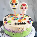 Dia De Los Muertos Cake with Sugar Skull Topper on a cake stand.