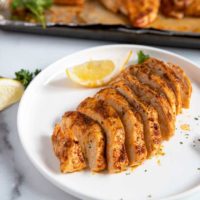 Oven baked and sliced chicken breast on a white plate.