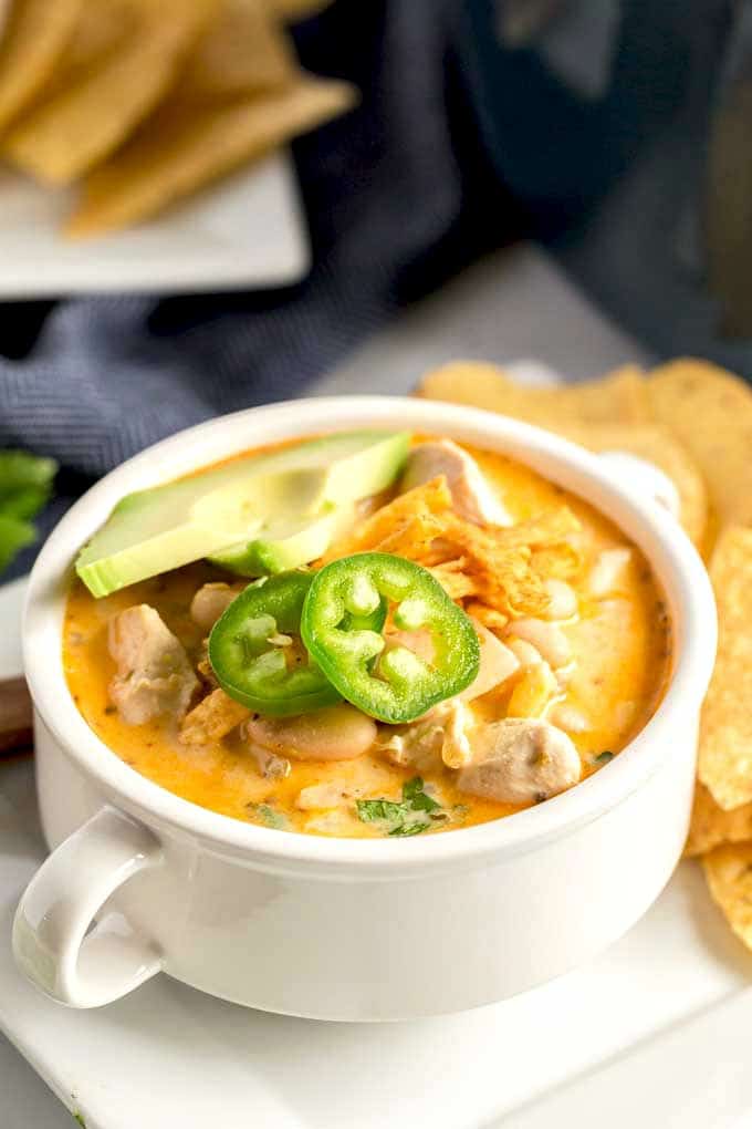 White Chicken Chili served in a white bowl and topped with cheese, tortilla chips and jalapenos.