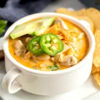 White Chicken Chili served in a white bowl and topped with cheese, tortilla chips and jalapenos.