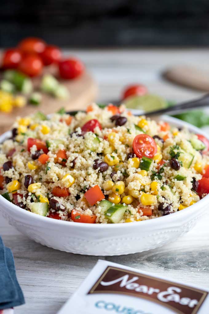 Couscous salad with tomatoes, cucumbers, corn and bell peppers in a white bowl.