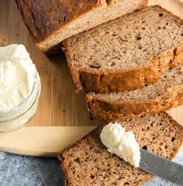 loaf of banana bread sliced served next to a small container of whipped butter,