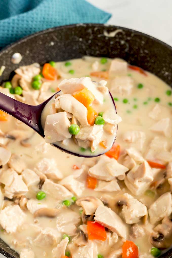Creamy chicken and vegetables in a skillet served with ladle