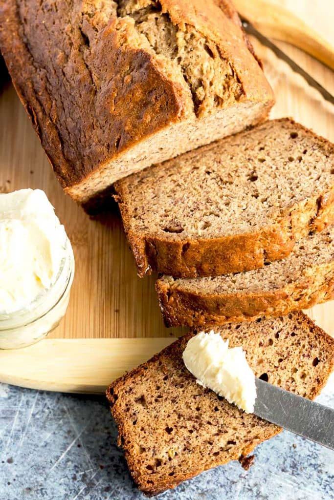 loaf of banana bread sliced served next to a small container of whipped butter