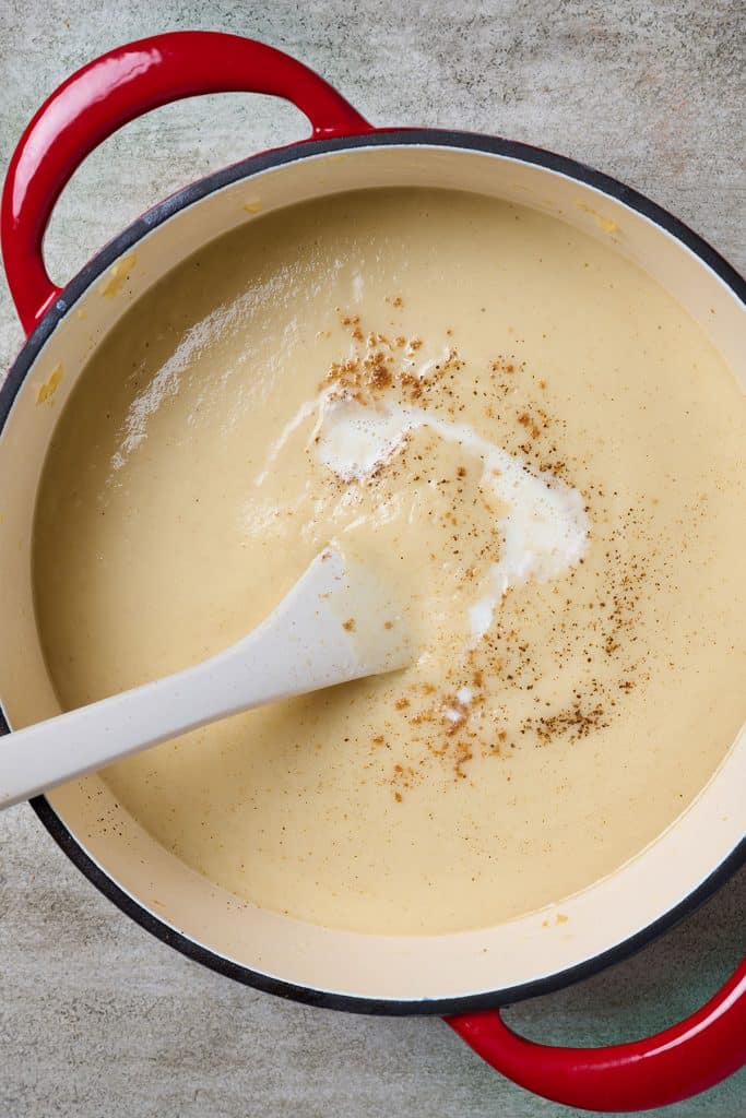 Creamy soup in a Dutch oven drizzled with plant-based milk and nutmeg