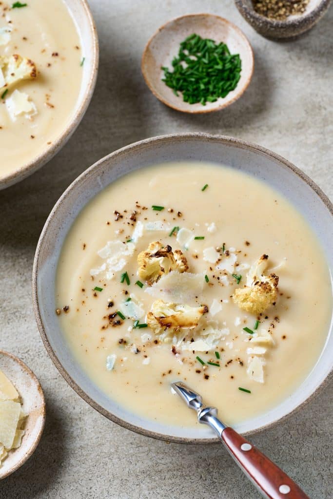 Creamy roasted cauliflower soup garnished with roasted cauliflower florets served in a soup bowl.