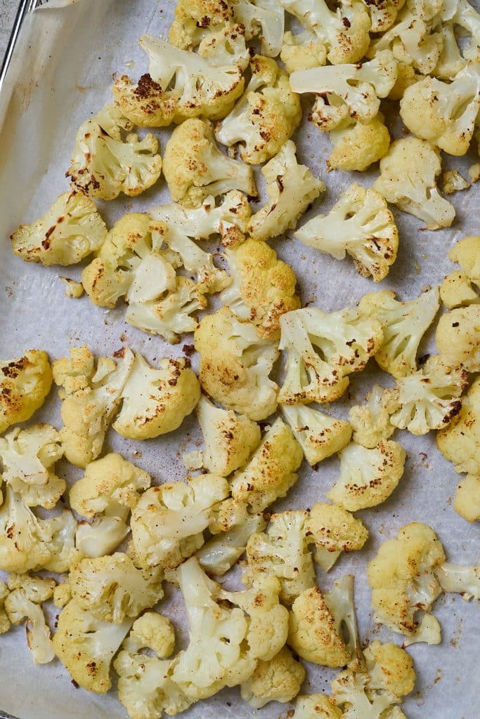 Golden brown roasted cauliflower on a baking pan lined with parchment paper.