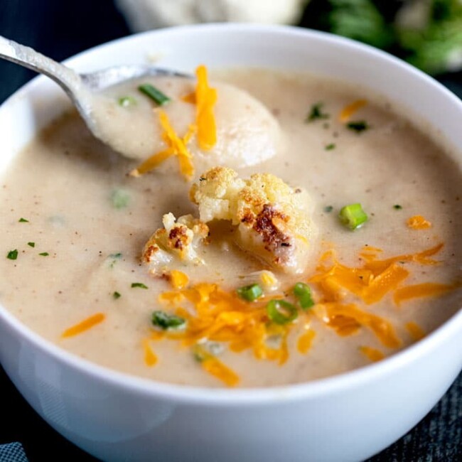 Creamy Cauliflower Soup topped with roasted cauliflower, shredded cheese and scallions
