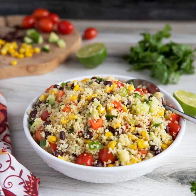 Couscous salad with tomatoes, cucumbers, corn and bell peppers in a white bowl.