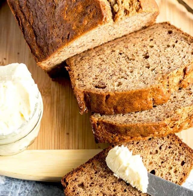 loaf of banana bread sliced served next to a small container of whipped butter