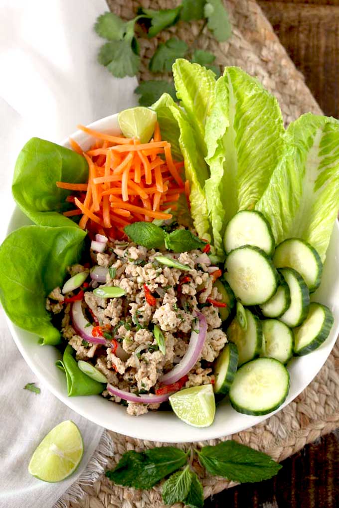 A bowl filled with ground chicken larb salad with lettuce leaves, cucumbers and carrots