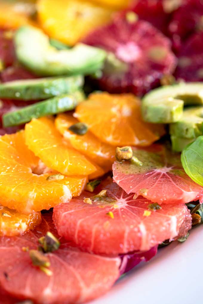 close up view of Peeled and sliced citrus fruit, oranges, grapefruit, pomelos with avocado slices and basil leaves on a white plate.