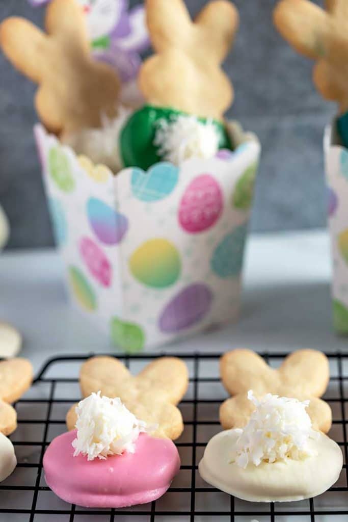 two bunny shortbread cookies over a cooling rack next to a colorful box filled with cookies