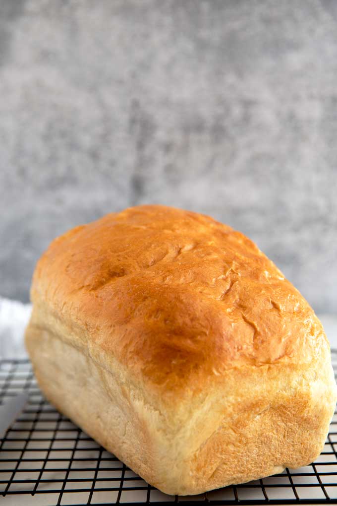 A loaf of homemade white bread on a cooling rack,