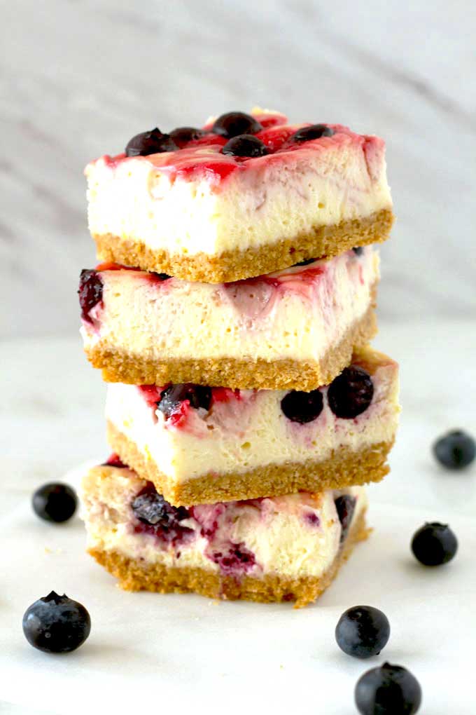 A stack of berry swirl cheesecake bars on a white kitchen surface.