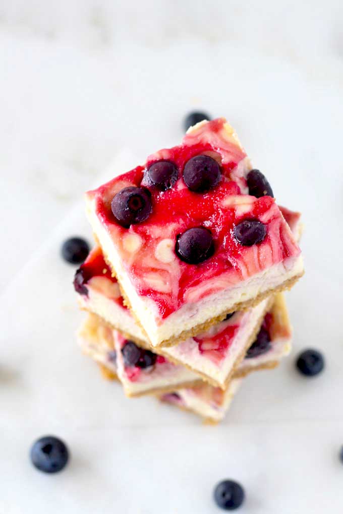 Top view of a stack of cheesecake bars with blueberries and raspberry swirl.