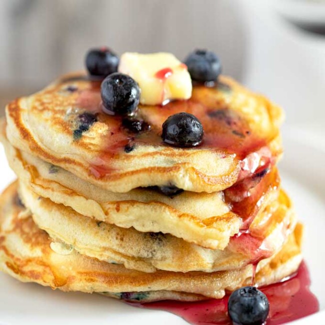 Fluffy Blueberry Pancakes Stacked up and drizzled with blueberry syrup.